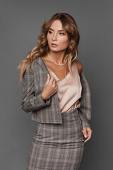 Elegant business lady in the checkered suit and satin blouse looking aside and posing on the gray background, isolated.