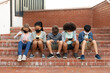 © Wavebreak Media - Group of kids wearing face masks using smartphones while sitting on the stairs together