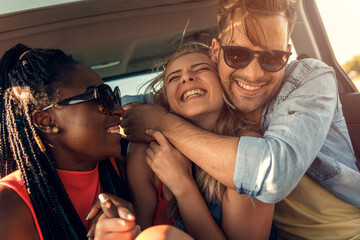 Wall Mural - Three best friends enjoying traveling in the car, sitting in rear seat and having lots of fun on a road trip.