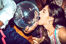 Young Woman With Eyes Closed Holding Drink And Biting Disco Ball In Glamorous Party