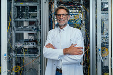 Smiling Mature Man With Arms Crossed Standing In Server Room