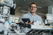 Smiling Male Scientist Holding Digital Tablet While Standing By Machinery In Laboratory