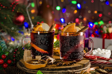 Mulled wine with orange slice, cinnamon stick on the background of festive garland lights. Dark style