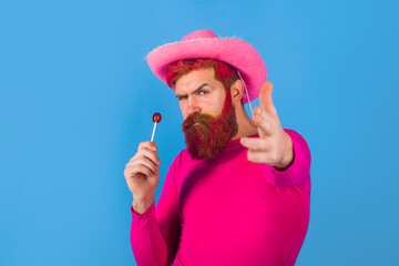 Gay. Homosexuality. Gay with lollipop. Portrait of gay cowboy. Man wearing cowboy hat. American bandit. Western man with hat. Pink velvet cowboy hat. Gay man. American West.