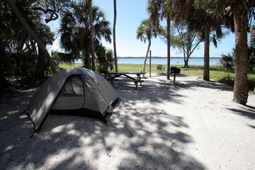 shady wooded tent camp site in fort de soto park in pinellas county, florida on beach and bay.