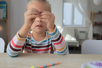 Little girl is making bracelet from beads