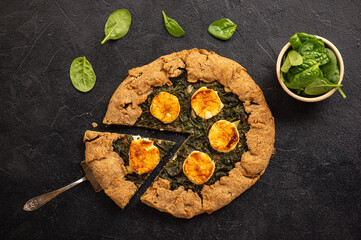 Wall Mural - Rustic spinach and goat cheese galette on black background.