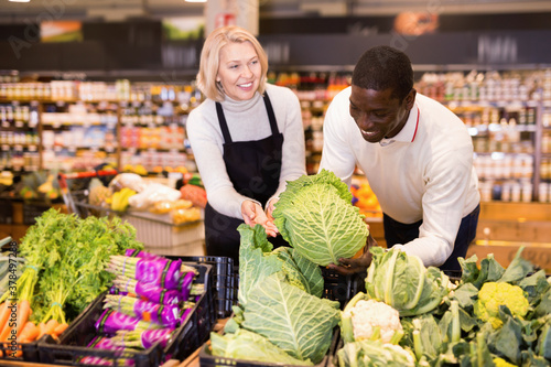 Fotomural Friendly cheerful positive glad middle aged saleswoman helping African man to ch