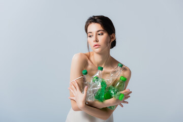 Wall Mural - brunette woman looking away and holding plastic bottles isolated on grey, ecology concept