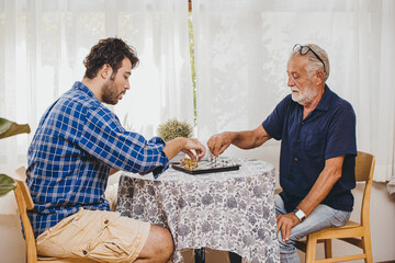 Smart old man playing chess board game with his son at home.