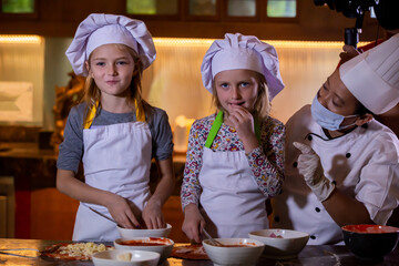 Wall Mural - Kid cooking class. Two little girls and teacher chef in kitchen during master class learning how to make pizza