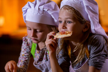 Wall Mural - Two little girls in chef hats eating pizza after cooking master class