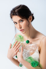 Wall Mural - brunette woman holding plastic bottles and looking at camera isolated on white, ecology concept