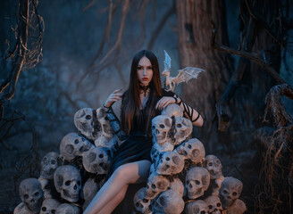 A beautiful sexy vampire woman sits on a throne of the skulls of her victims in a dark mystical forest. Gothic image of the goddess of death with white dragon. dark queen on the hill of skeletons.