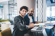 © BullRun - Portrait of cheerful male professionals smiling at camera during collaborative meeting for developing business project, Middle Eastern executive managers using laptop computer and textbook documents