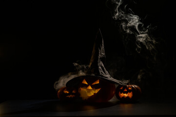 Wall Mural - Three jack o lanterns glow in the dark amidst the fog. Halloween pumpkin in a witch hat.