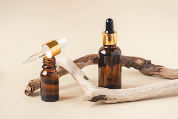 Two brown bottles of cosmetics on a beige background. Natural driftwood decor. Front view.