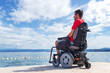 © 24K-Production - Man with muscular dystrophy on electric wheelchair outdoors looking at sea.