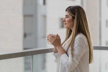 young woman thinking and looking away with cup of tea or coffee with blurred city background. girl d