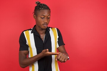 Wall Mural - African american man with braids wearing casual shirt over isolated red background In hurry pointing to watch time, impatience, upset and angry for deadline delay.