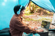 Smiling Asian people wearing headphones listening podcast music online on a laptop  he is sitting in the tent vacation relaxing outdoor
