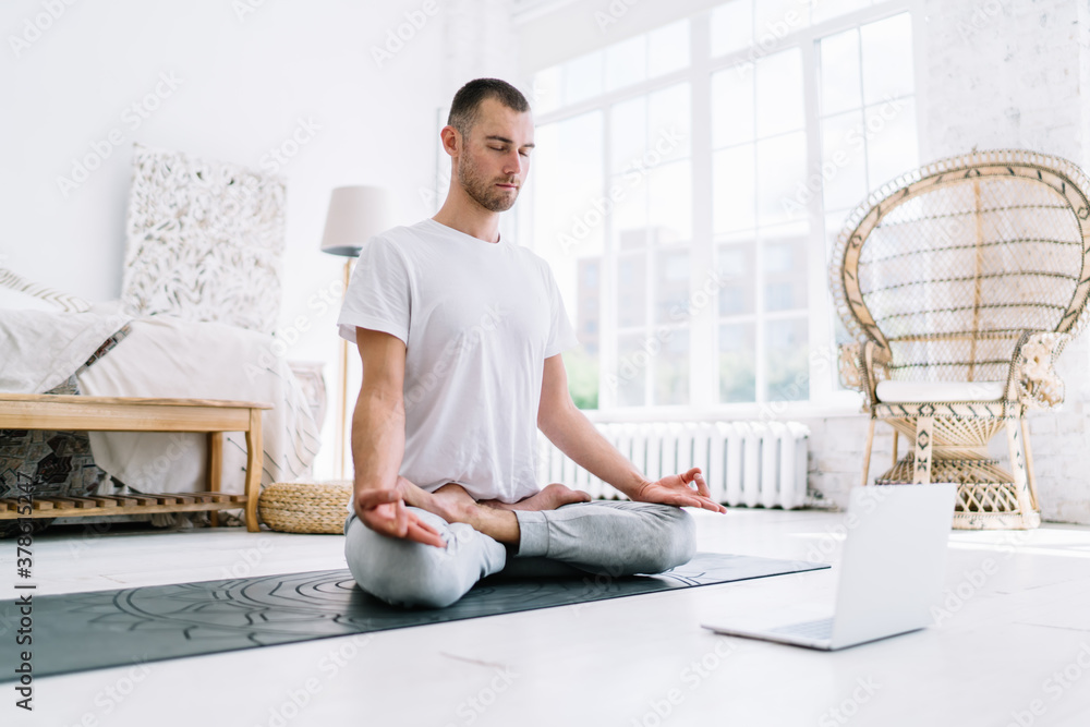 Calm tranquil caucasian male with closed eyes enjoying meditation using laptop computer for listening online lesson, man spending time on spirituality and healthy lifestyle practice yoga at home - obrazy, fototapety, plakaty 
