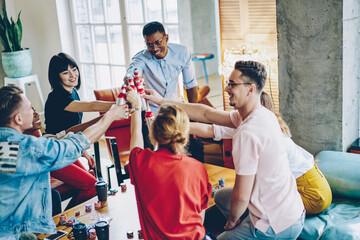 Happy multicultural people dressed in casual wear clicking with alcohol drinks celebrating friendly bonding meeting party for playing poker or blackjack game in modern home apartment, Cheers!