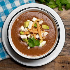 Mexican cream of bean soup with avocado and cheese on wooden background