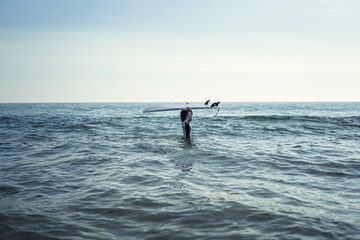 Sticker - Young female in a swimsuit holding a surfboard in the sea