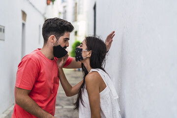 Poster - Shallow focus of a young couple in facemasks embracing each other against a wall