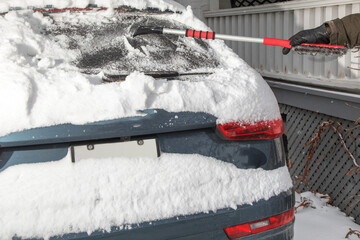 winter driving safety - a driver clearing fresh snow from the rear window to be able to see traffic behind