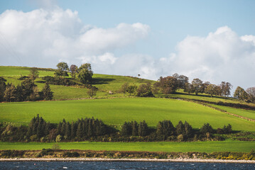 Wall Mural - Green hills near Firth of Clyde river, panoramic view from a sailing boat. Dramatic sky after the storm. Scotland, UK. Travel destinations, eco tourism, vacations, pure nature. Atmospheric landscape