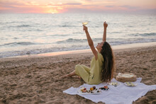 Young Beautiful Woman Having Picnic With Wine, Pizza, Cheese And Fresh Fruits On Beach  At Sunset.