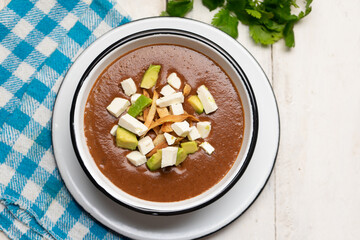 Mexican cream of bean soup with avocado and cheese on white background