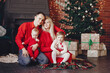 © hetmanstock2 - Beautiful mother in a red dress. Family sitting near christmas gifts. Little girl and boy near christmas tree