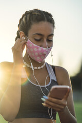 Sticker - Vertical shot of a woman listening to music on her phone while wearing a facemask