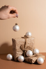 Wall Mural - The girl's hand keeping white christmas ball over the paper gift box and other small balls isolated on a beige background. Idea for holiday. Christmas concept.