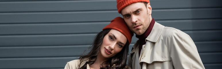 Wall Mural - horizontal crop of stylish couple in hats standing and looking at camera outside