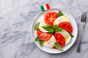 Wall Mural - Caprese salad with tomatoes, mozzarella cheese and basil with Italian flag. Marble background. Top view.