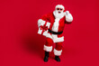 © deagreez - Full length photo of retired old man white beard walk hold box bow-knot gift christmas tree wear x-mas santa costume glove coat belt sunglass cap boot isolated red color background