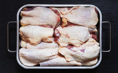 Wall Mural - Photography of raw, boneless chicken thighs in a metal bin on slate background for food illustrations