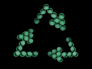 Closeup of green plastic bottle caps forming the recycling symbol isolated on a black background