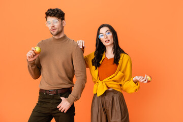 Wall Mural - trendy couple in glasses and autumn outfit holding apples isolated on orange