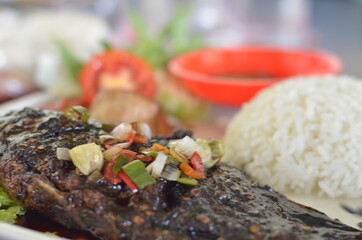 Large baked carp fish, indonesian traditional grilled carp fish. served on white plates in wooden board with sambal, soy sauce and other ingredients.