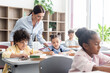 © LIGHTFIELD STUDIOS - Selective focus of teacher standing near multiethnic pupils during lesson in school