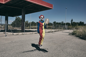 Wall Mural - scary clown with a golden balloon jumping outdoors