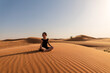 With eyes closed and a posture of tranquility, she is engaged in a deep state of meditation, harmonizing with the vast and quiet expanse of the desert