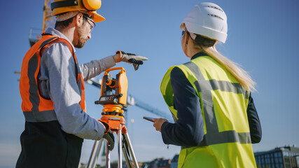 Wall Mural - Construction Worker Using Theodolite Surveying Optical Instrument for Measuring Angles in Horizontal and Vertical Planes on Construction Site. Engineer and Architect Using Tablet Next to Surveyor.