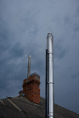 Metal smoke pipe and red brick chimney on sky background. Copy space.