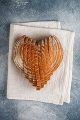 Wall Mural - Sliced round loaf of rye bread in the shape of a heart on a gray linen napkin. Tasty and usefull home baking product close-up. Selective focus